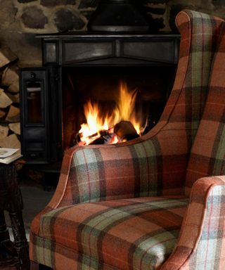 A living room with an orange and gray plaid armchair and a black fireplace with logs around it in the background