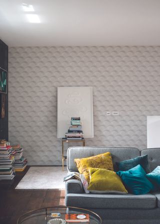 Arcade wallpaper in white living room with grey cotton couch, colored cushions and books on display