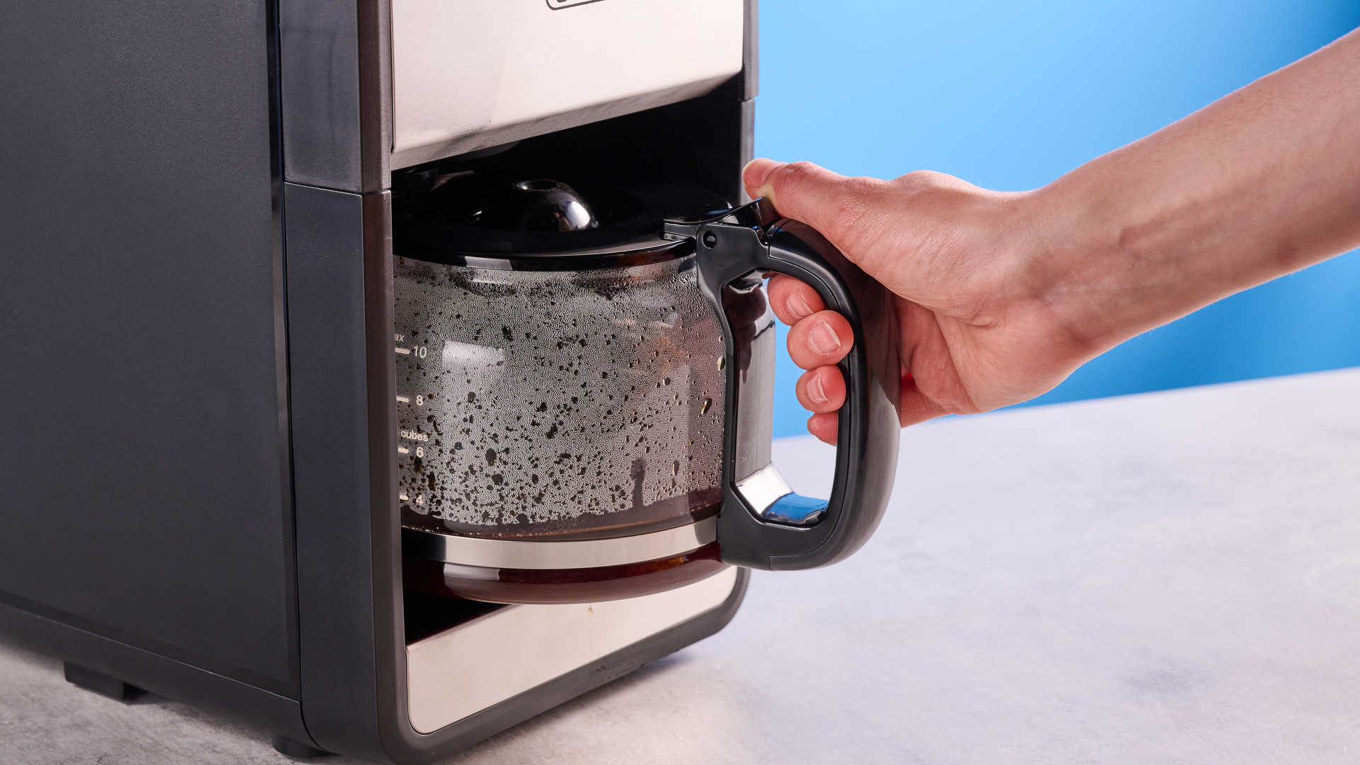 the gevi 10-cup drip coffee maker with grinder photographed against a blue background, showing the glass carafe, water tank, touch screen, and accessories including plastic filter