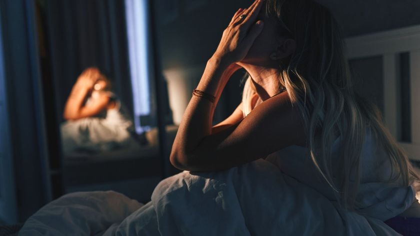 The image shows a blonde-haired woman sitting up in bed in the dark with her hands on her face