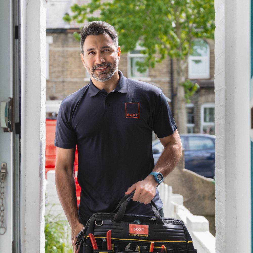 male with short dark hair and beard wearing blue polo shirt with BOXT logo stood in doorway with tool bag