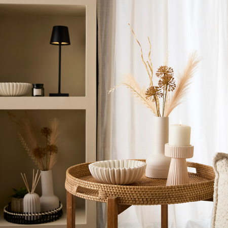 The viral fluted bowl on a rattan side table. Next to it is a soft neutral vase with dried flowers and a ribbed candle holder.