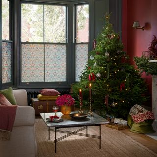 Red living room with Christmas tree decorated with green and red ribbons, window film, presents under tree, coir rug, square coffee table