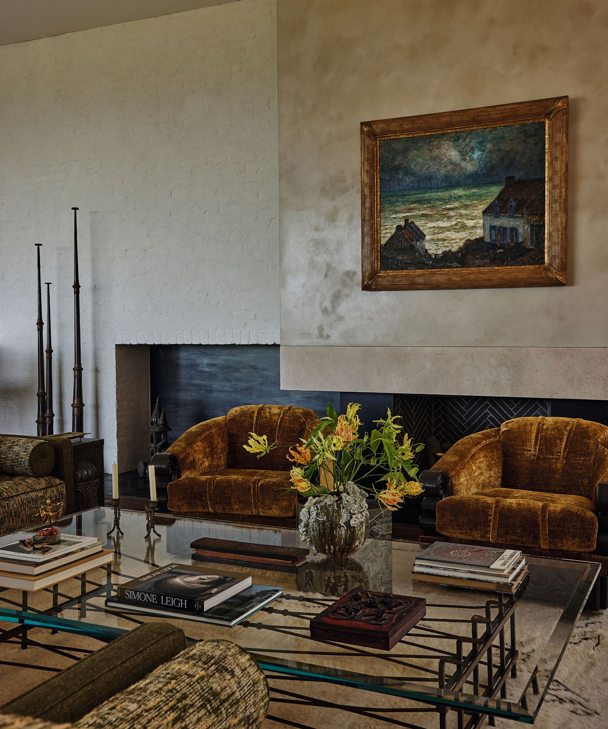Living room with two amber velvet armchairs, a glass coffee table, and a large framed oil painting hanging above a sleek modern fireplace