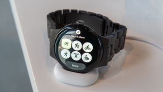 Pixel Watch 4 on the charger showing the Fitbit Quick Start Tile