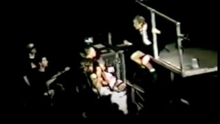 Angus Young sitting on the edge of the stage beckoning a fan over