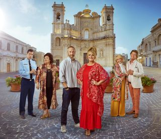 The Madame Blanc Mysteries season 3 cast in a group shot set against the backdrop of Sainte Victoire's main square: Alex Gaumond as Caron, Sue Vincent as Gloria, Steve Edge as Dom, Sally Lindsay as Jean, Sue Holderness as Judith and Robin Askwith as Jeremy