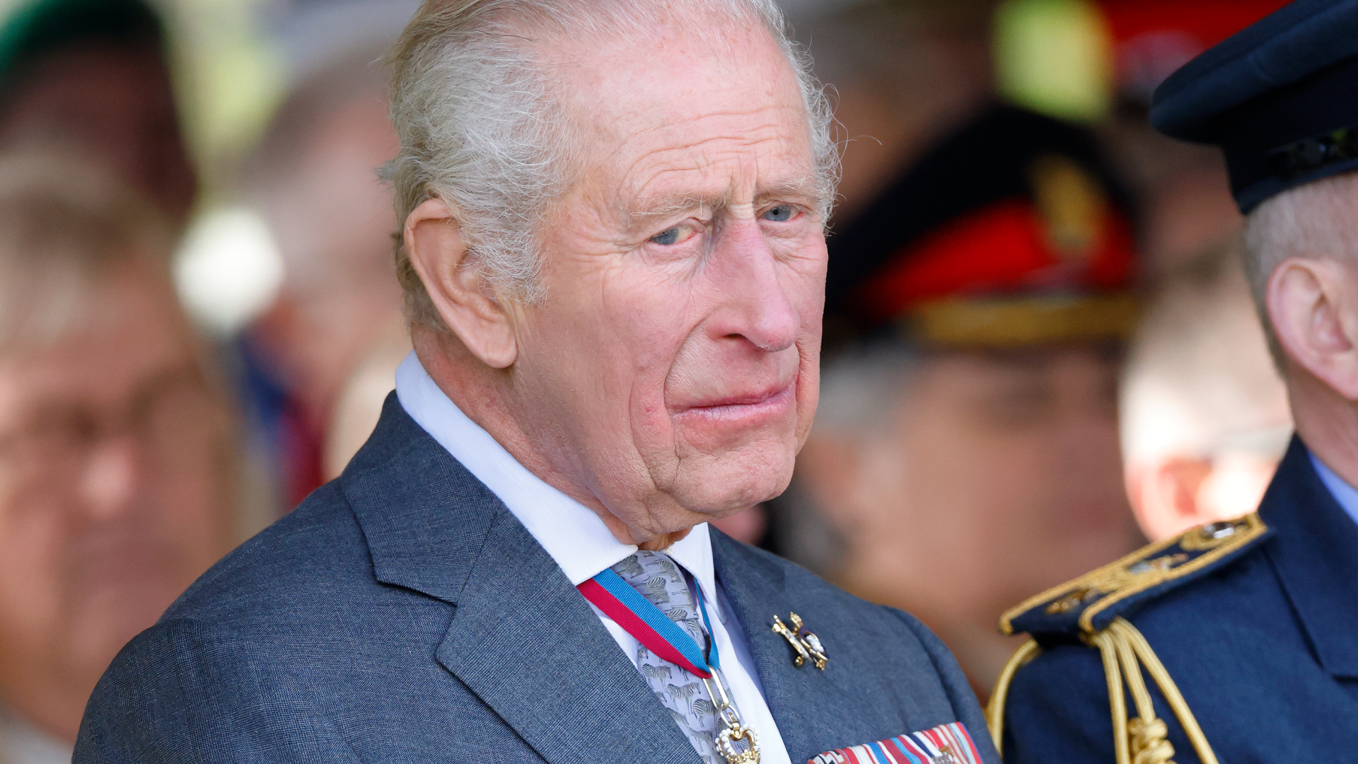 King Charles wears a blue suit with military medals attached and he looks very sad