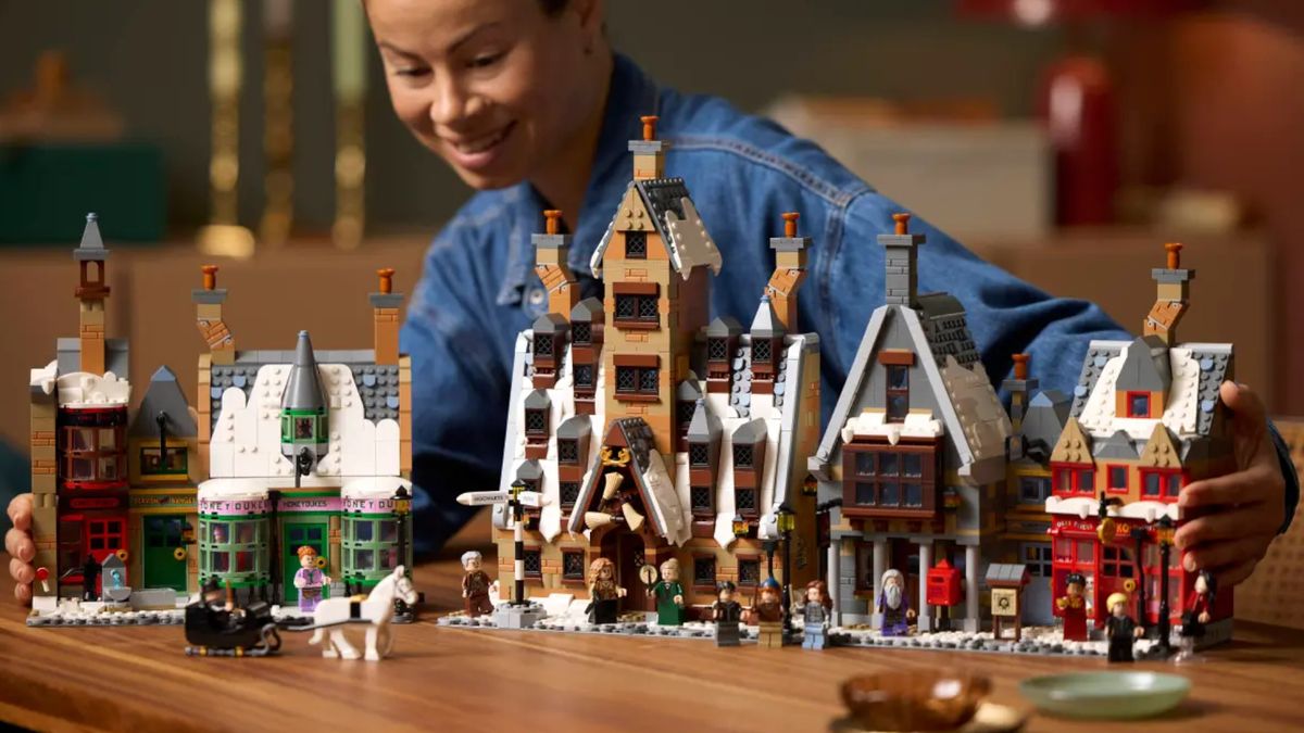 A woman smiles while holding the Lego Hogsmeade Village - Collectors' Edition set, which stands on a wooden table