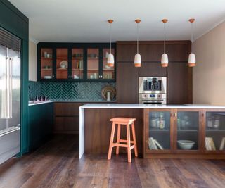 Green and wood kitchen with a pop of pink through the decor and insides of the glass-fronted cabinets