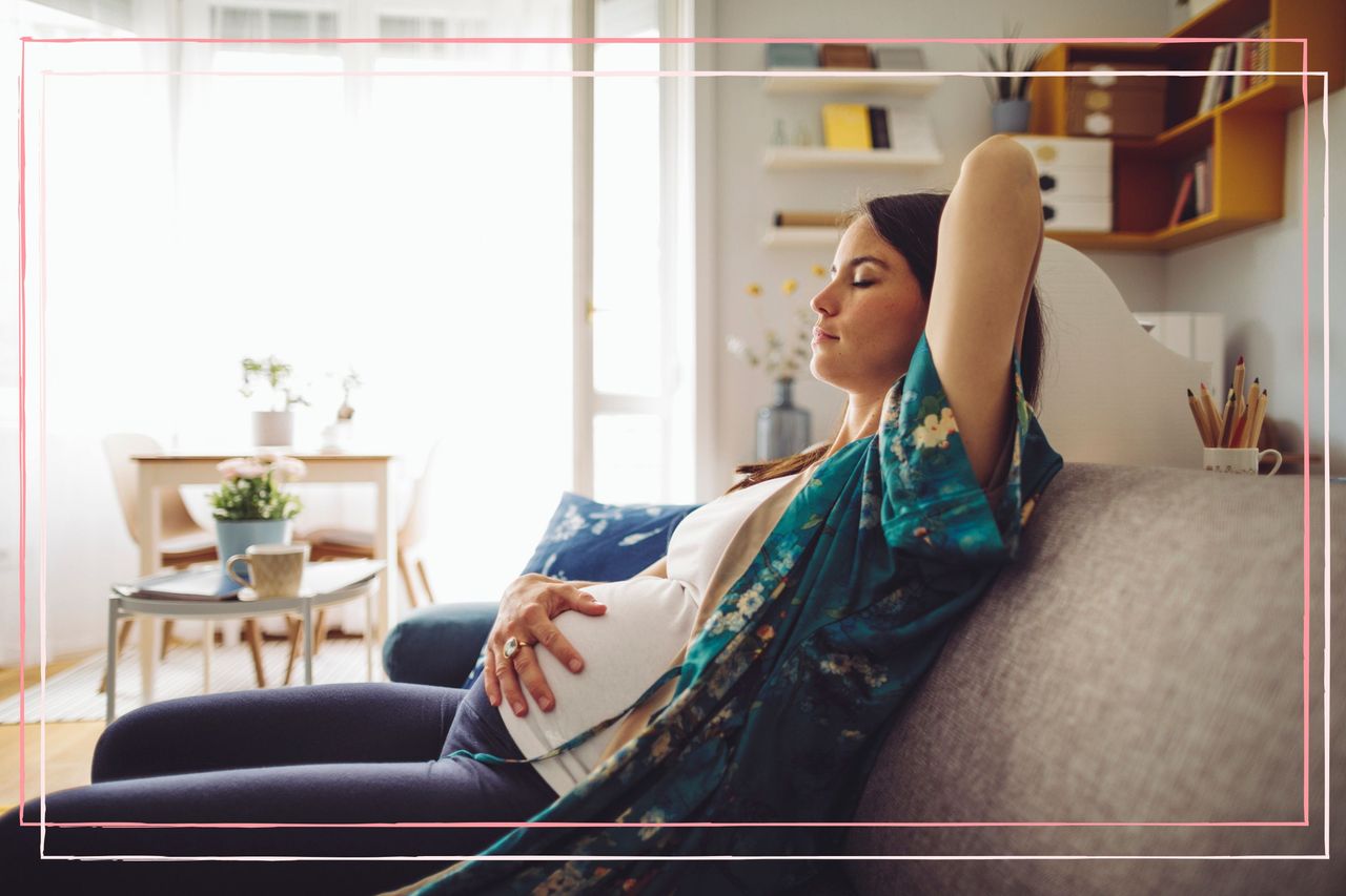 A pregnant woman on the sofa with her eyes closed whilst experiencing pregnancy headaches