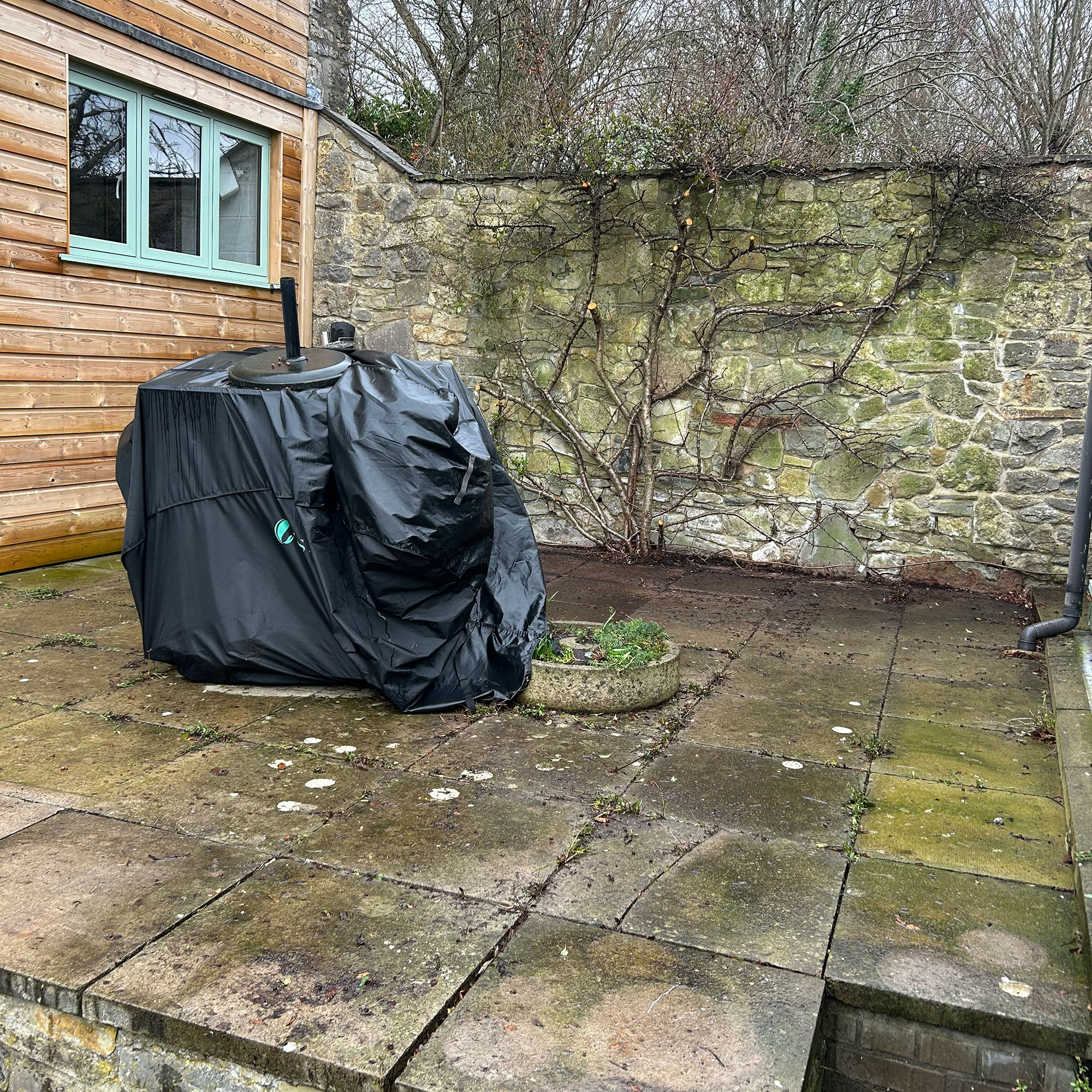 Stone wall enclosed patio with mossy slabs and covered BBQ