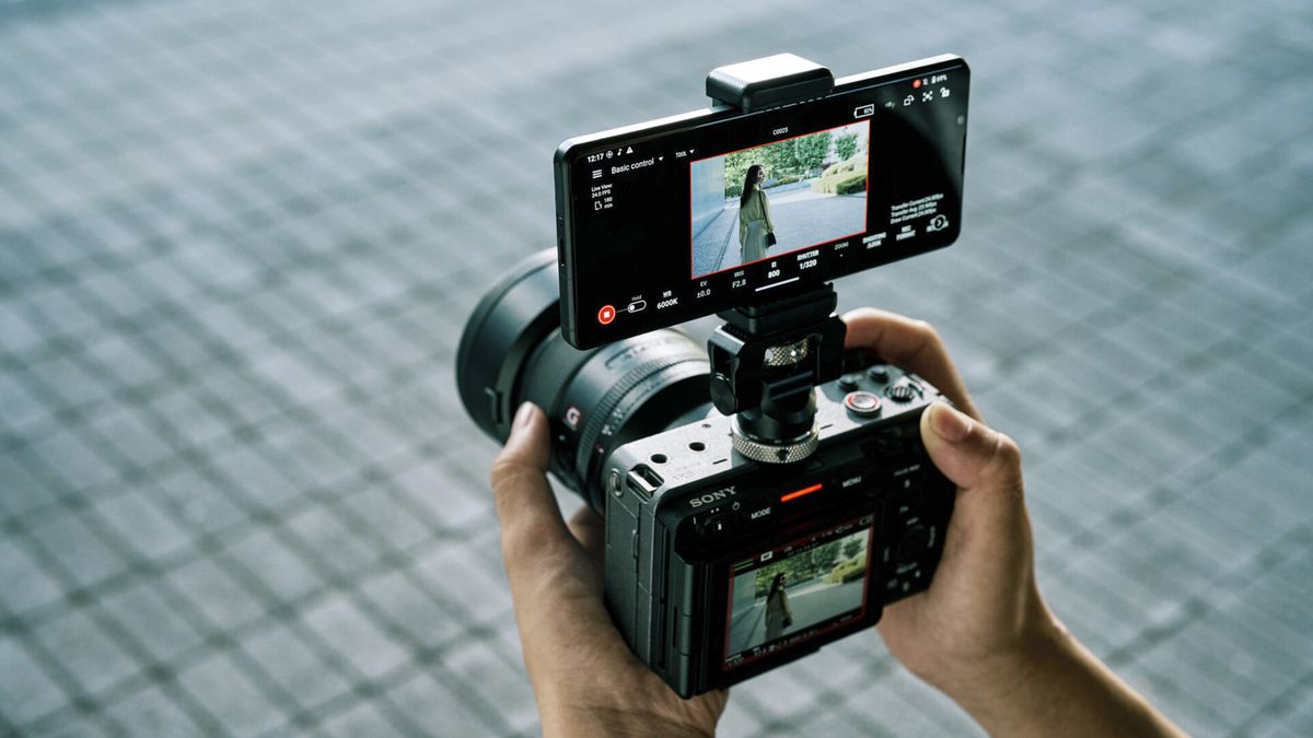 Videographer holding Sony cine camera with smartphone attached above with Sony Monitor &amp; Control app active, displaying the frame