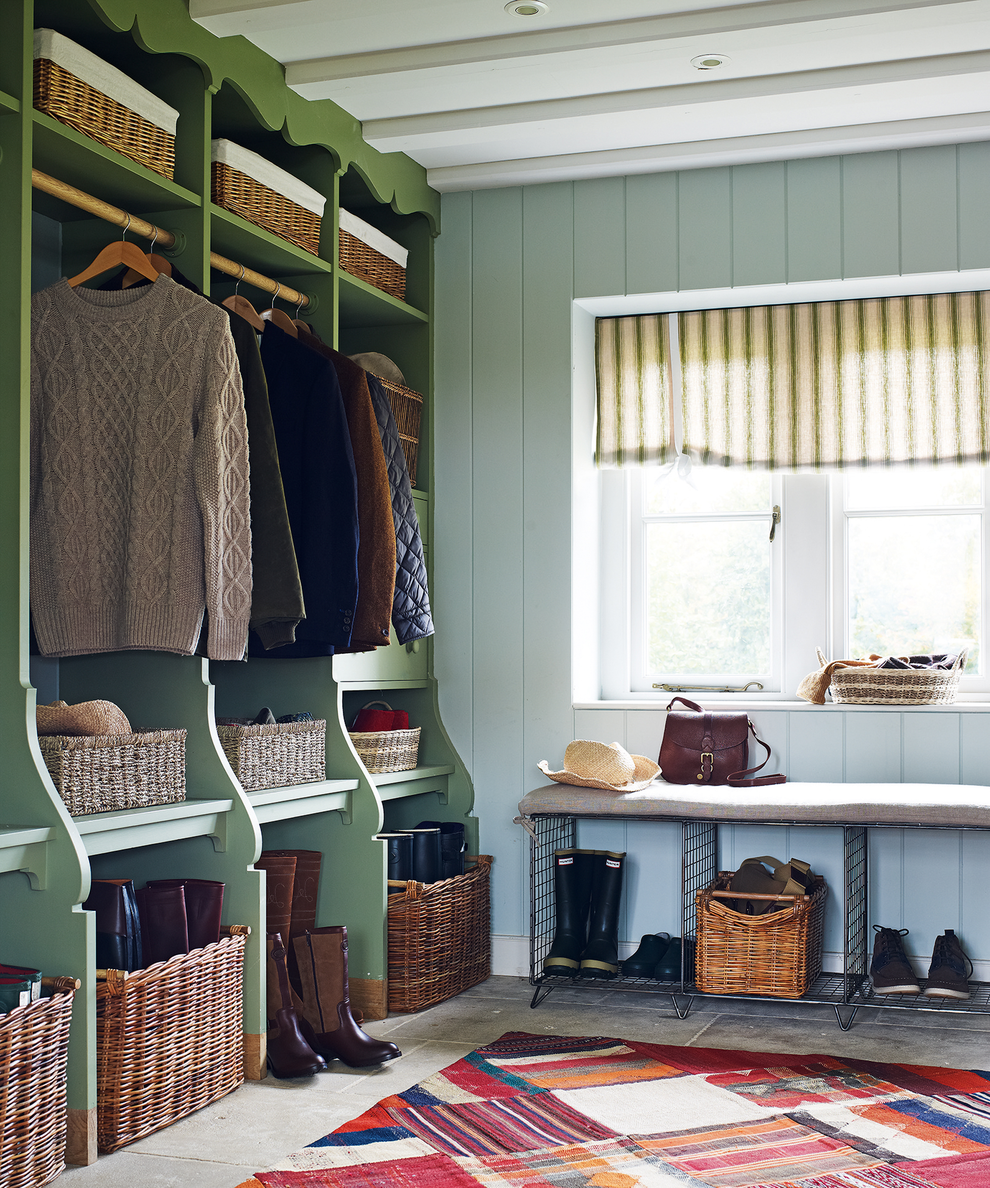 A mudroom with a green open shelving unit divided into personal sections, and woven baskets for boots