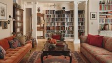 Spacious living room with orange and patterned red sofas, a dark wood coffee table, and classical white columns in front of floor-to-ceiling bookshelves.