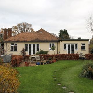 Green garden with stepping stones in front of cream coloured bungalow with red roof