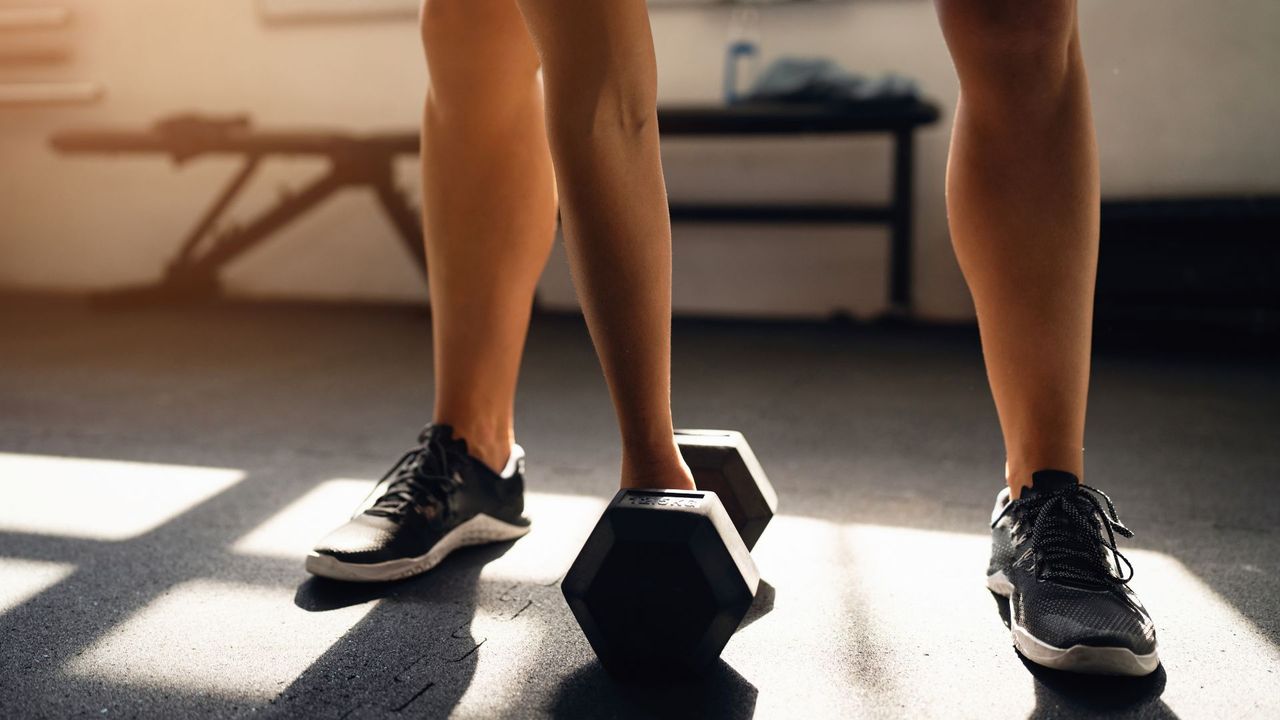 Someone leaning down to pick a dumbbell up off of the floor