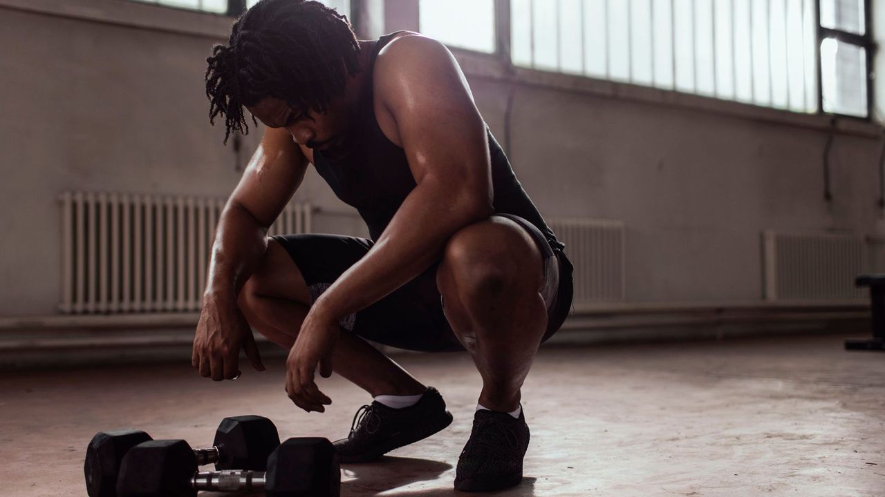 Man standing tired over a pair of dumbbells in the gym