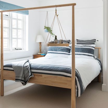 bedroom with white wall and bedding with white cushion and throw with grey strips and bedside table with lamp