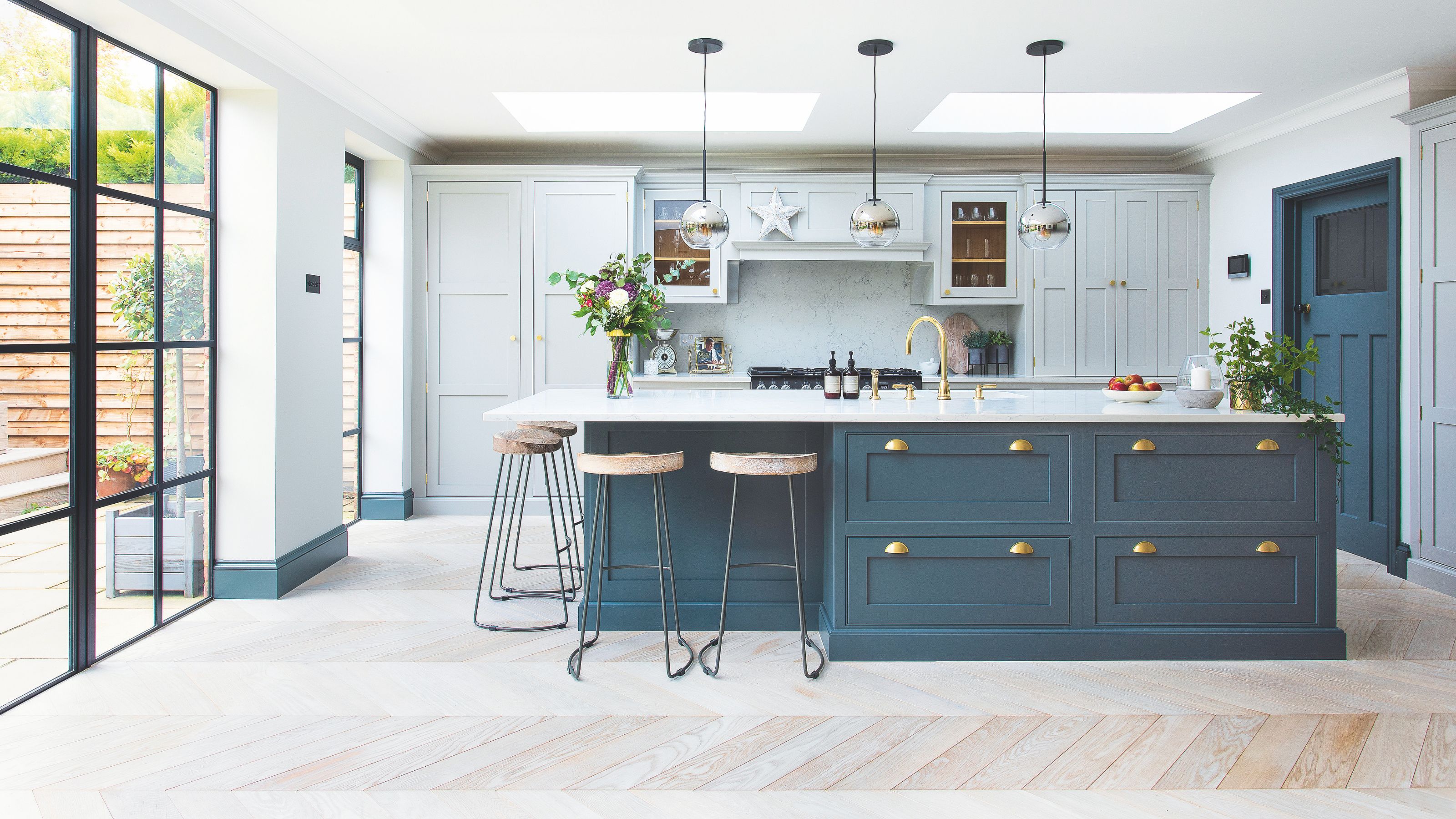White kitchen with wooden floor, a kitchen island with blue cabinets and bar stools around it