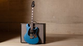 A lifestyle press image of the Sterling By Music Man StingRay Baritone SR50 in Toluca Lake Blue leaning against a Marshall amp in an empty room with concrete walls