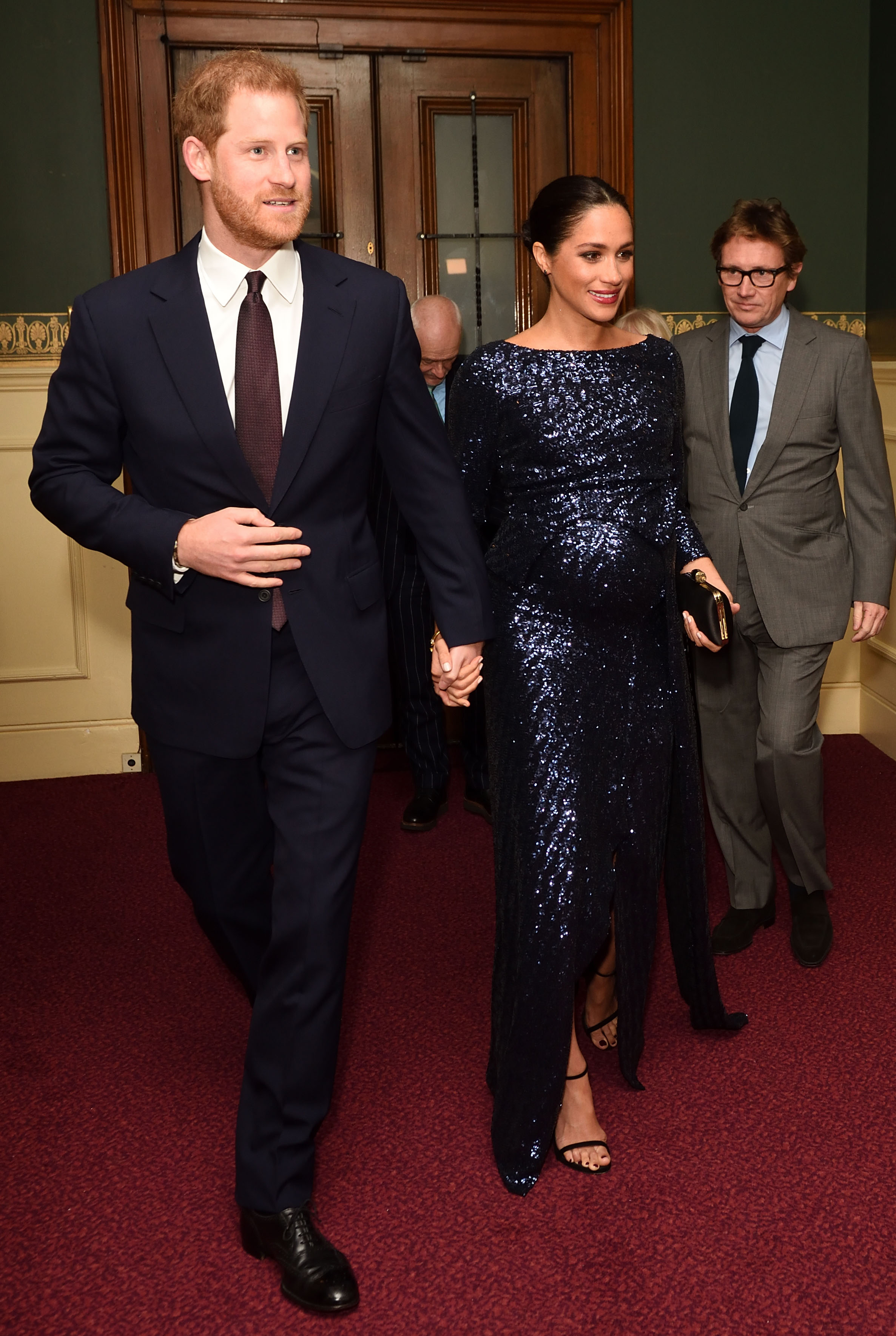 Meghan Markle holding hands with Prince Harry, wearing a blue sequined gown