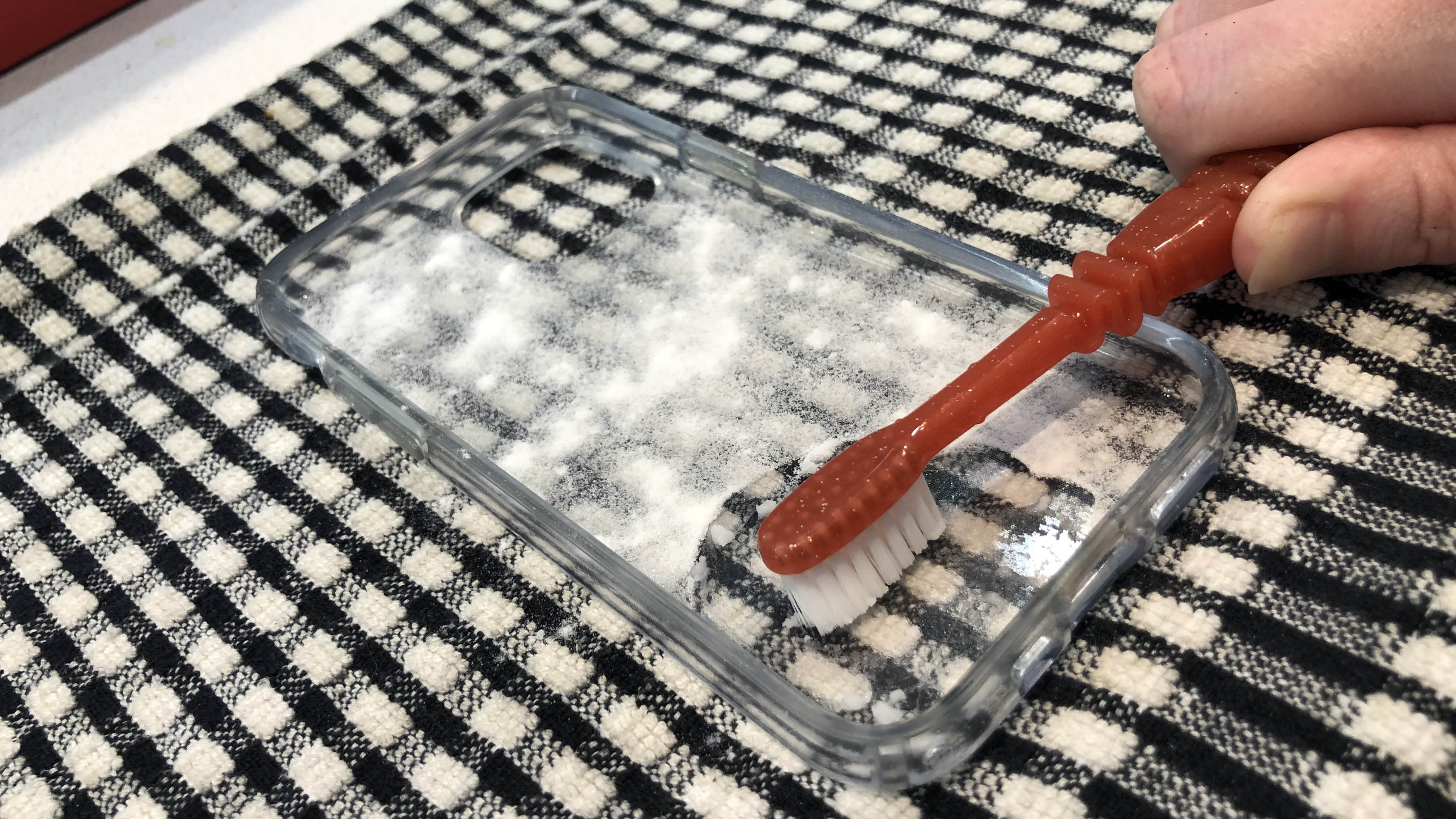 A clear phone case sitting on a towel being cleaned with baking soda and a toothbrush