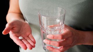 A person holds a pill in one hand and a glass of water in the other hand.