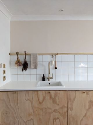 White kitchen sink with hanging utensils and white tiling under half painted wall