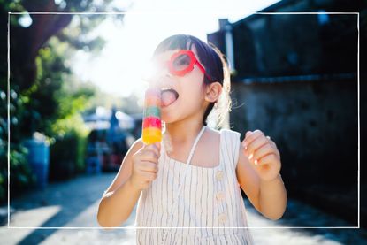 young girl in red sunglasses and summer dress eating an ice lolly