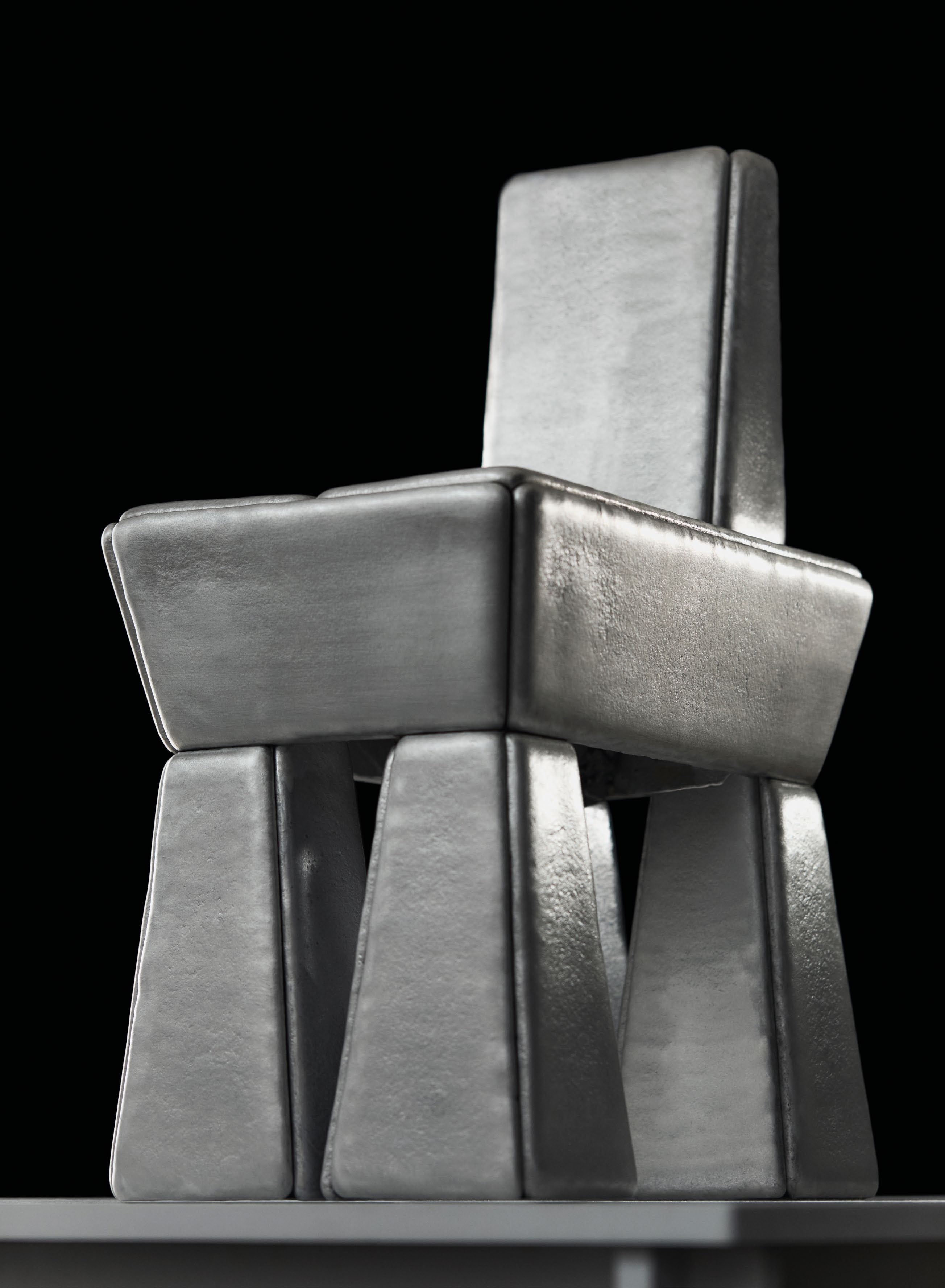 A sculptural chair made from cast aluminium, featuring a geometric design with a playful inflated quality, as described in the article 'MATERIAL ALCHEMISTS' by Wallpaper.
