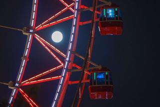 close up of a red Ferris wheel with lights on and a full moon shining behind.