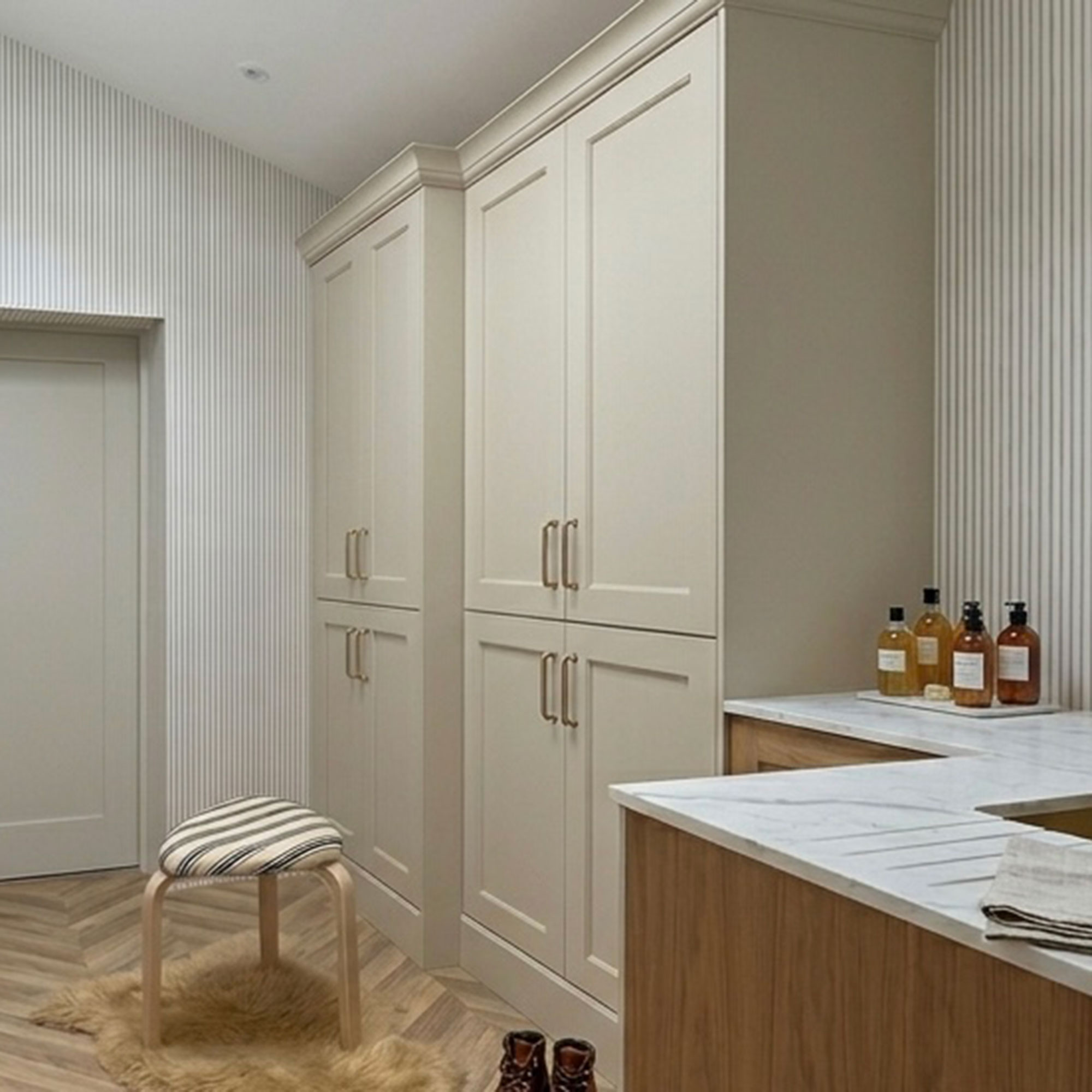 AI image of neutral utility room with striped walls, cream cabinetry, wooden flooring and upholstered stool