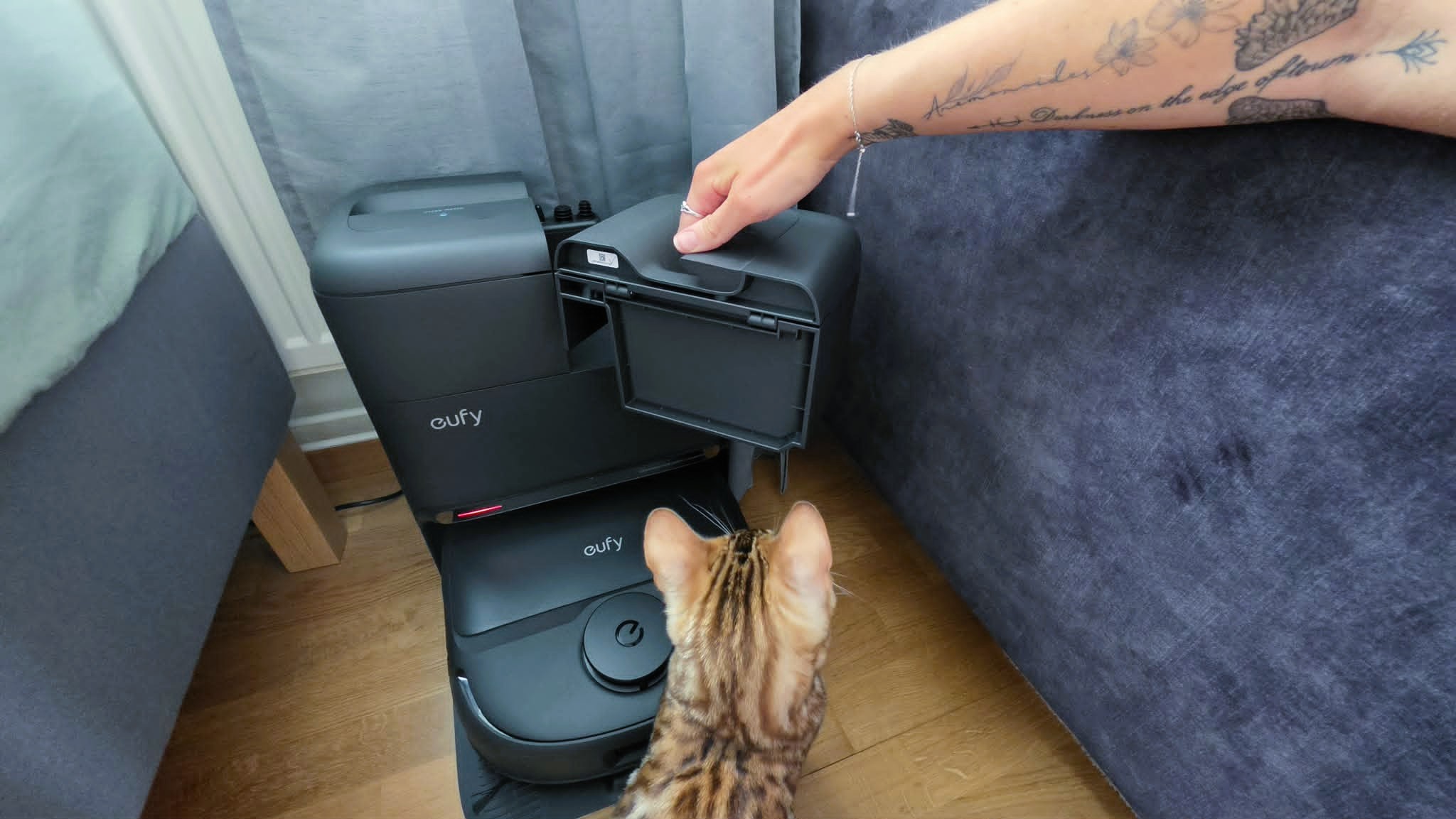 En hand lyfter upp den ena vattentanken till Eufy C28, med en bengalkatt bredvid som kollar p&amp;aring;.