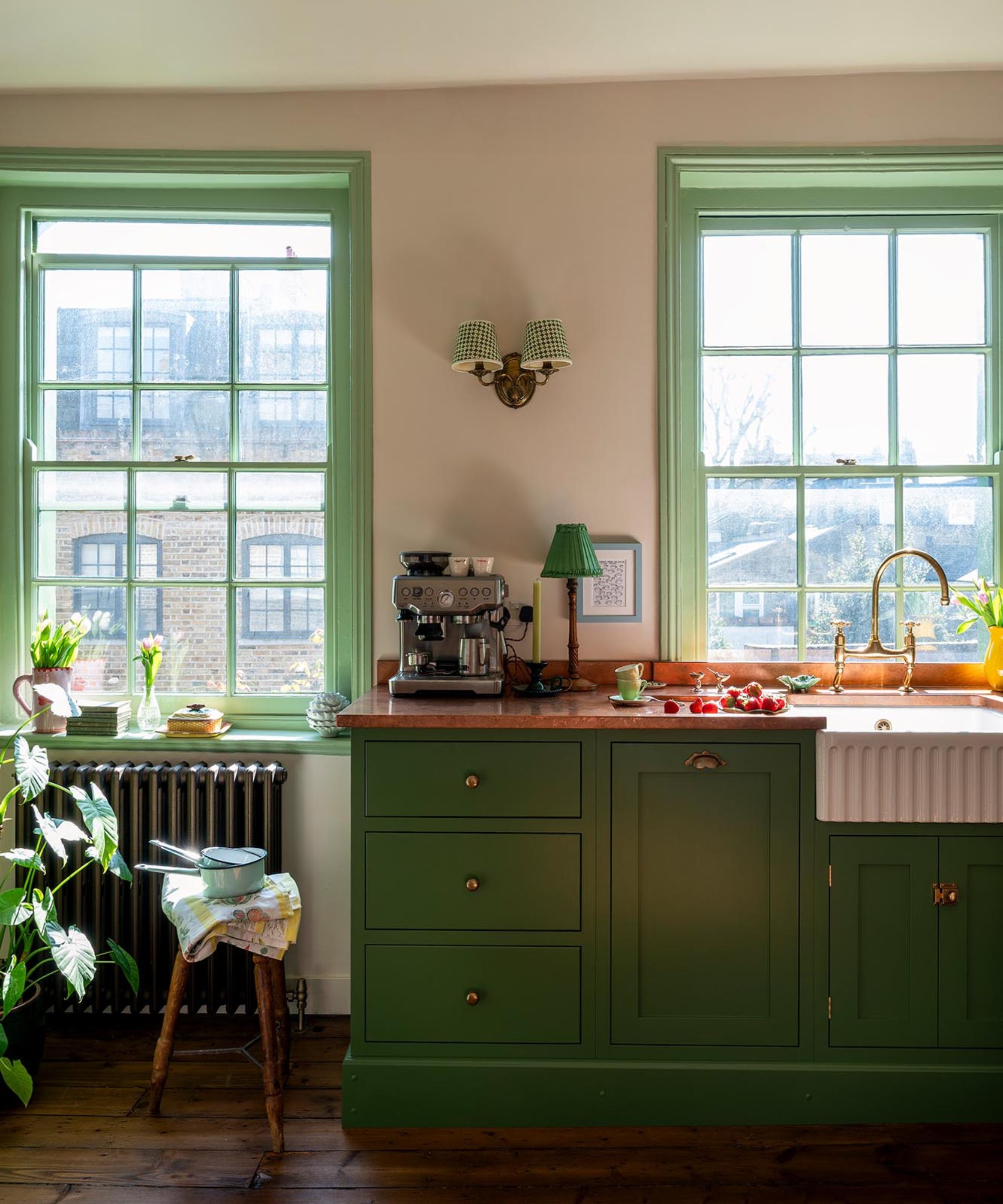 A small green kitchen with shaker cabinets, copper countertops, a stainless steel coffee machine, and layered lighting