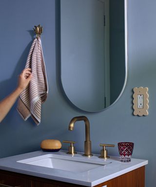 blue wall in bathroom with modern sink and curved wall mirror and hand towel hung on wall