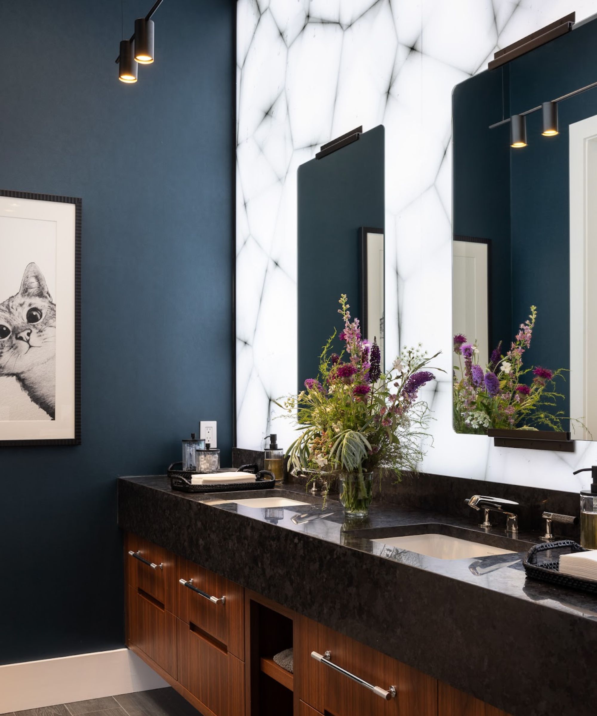 A guest bedroom with dark blue walls, a wooden vanity with a black countertop, a light-up wall, and a artwork of a cat framed on the wall