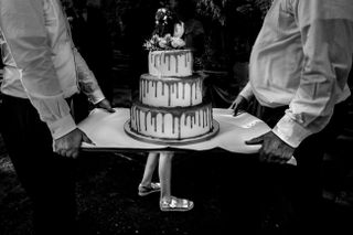 Two men carrying a wedding cake made to look like a child is poking out of it