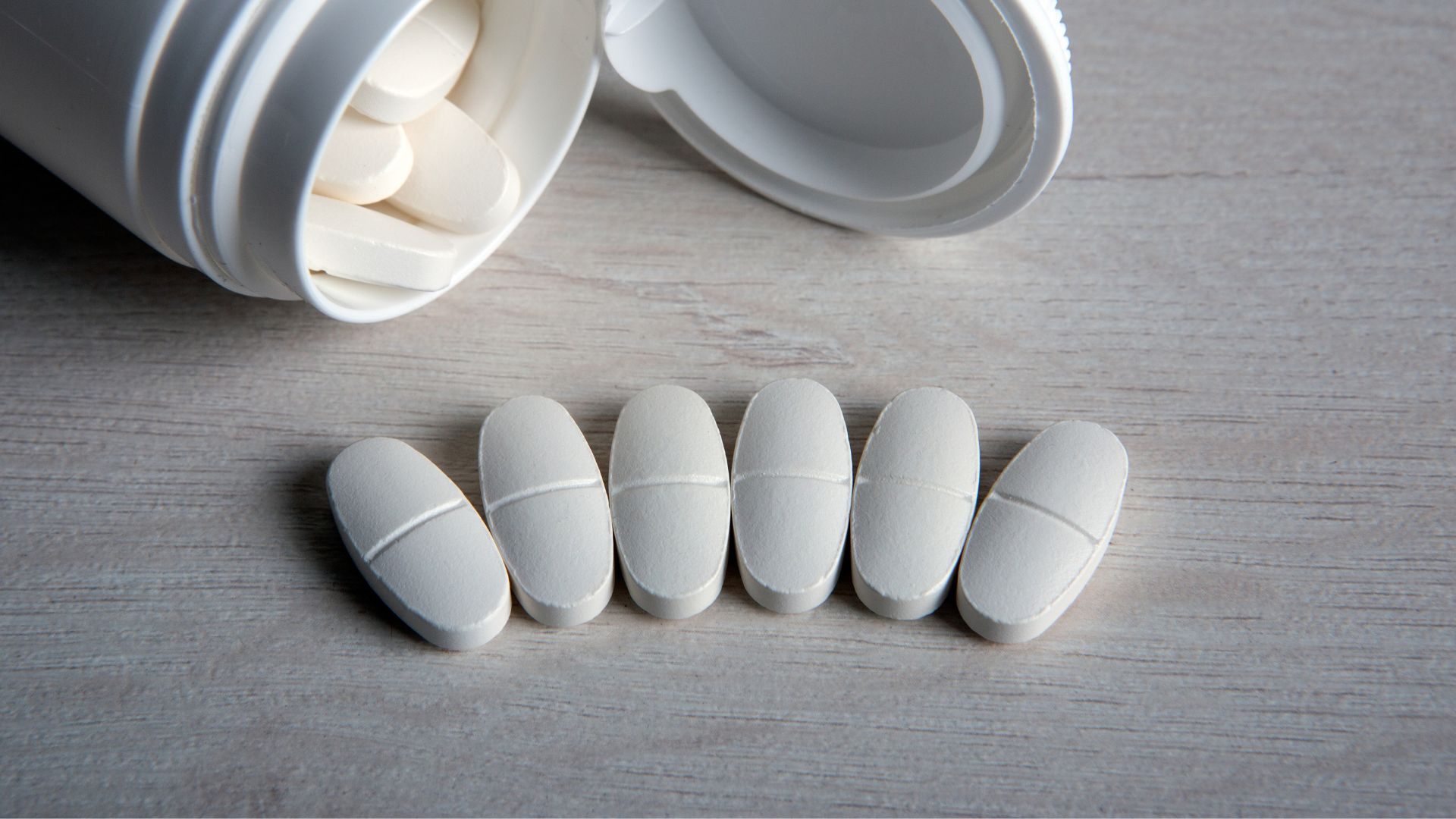 An open jar of calcium supplements beside a row of six tablets.