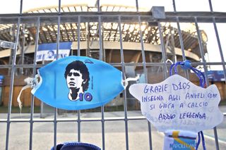 A sign which reads 'Thank you God, teach the angels how to play football, farewell legend” hangs next to a Diego Maradona face mask on the gates of Napoli's San Paolo stadium