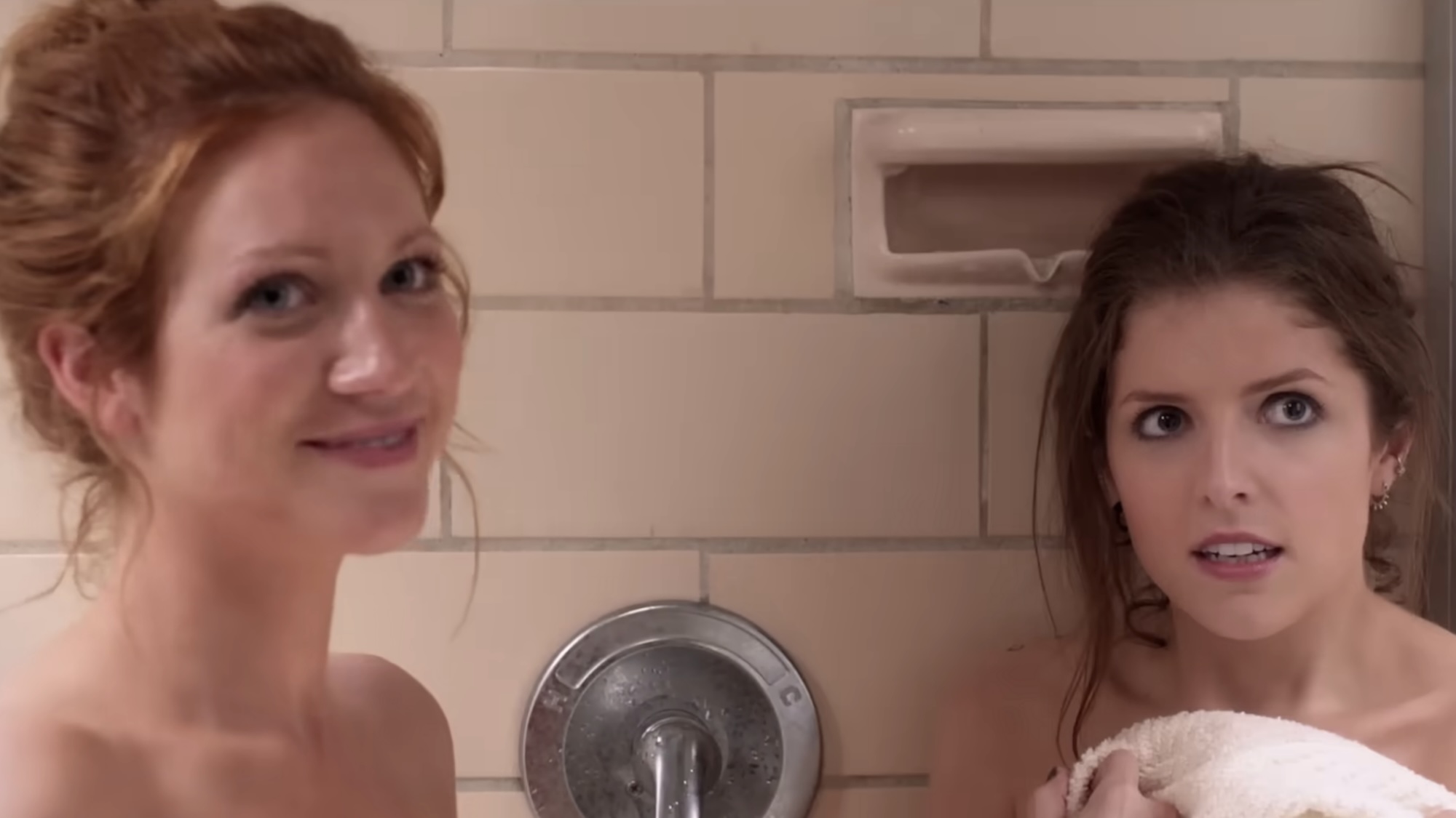 Brittany Snow smiling and Anna Kendrick looking annoyed during Pitch Perfect's shower scene. 