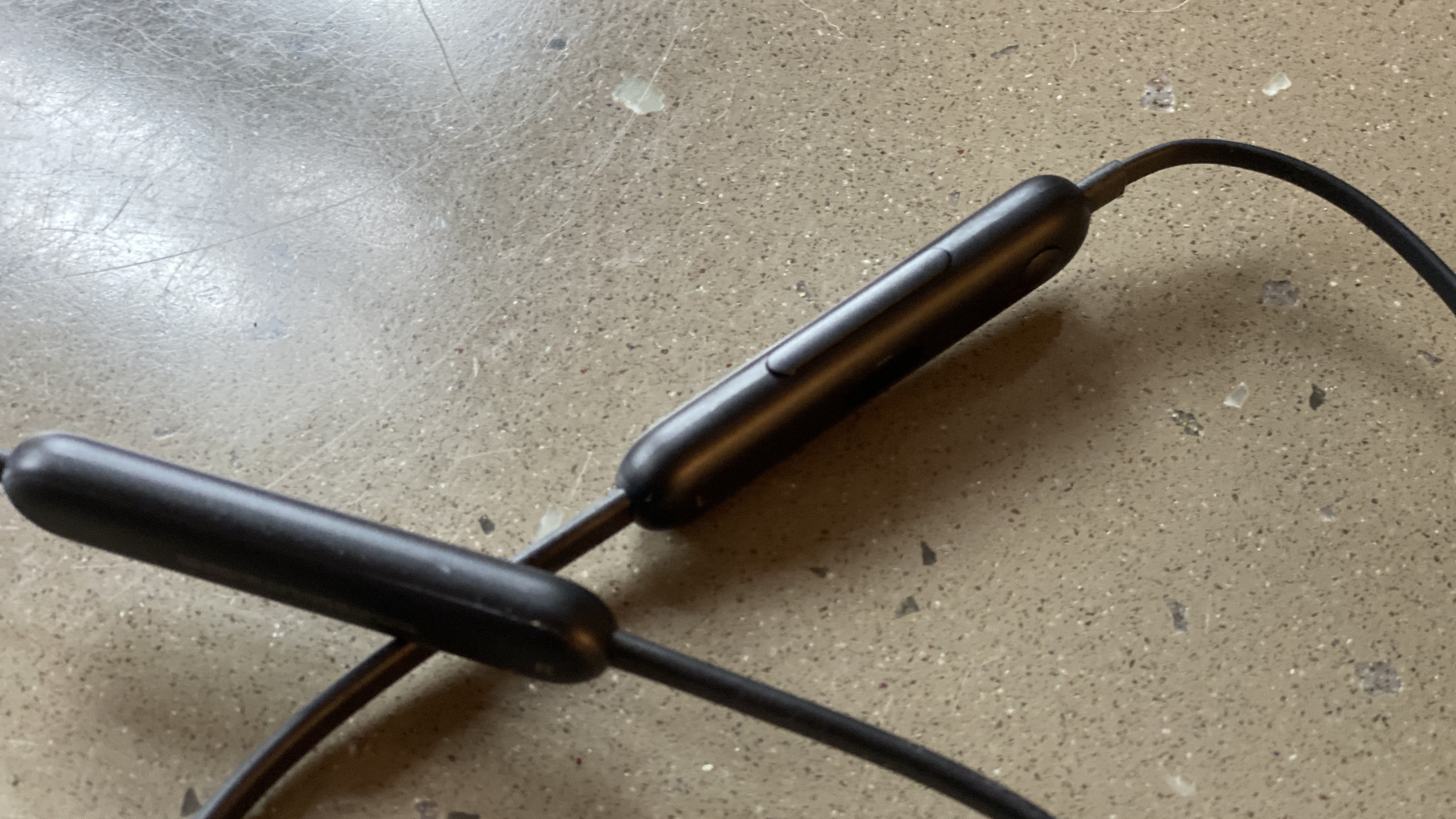 Tampilan dekat kontrol earphone nirkabel Beats Flex berwarna hitam di atas permukaan marmer