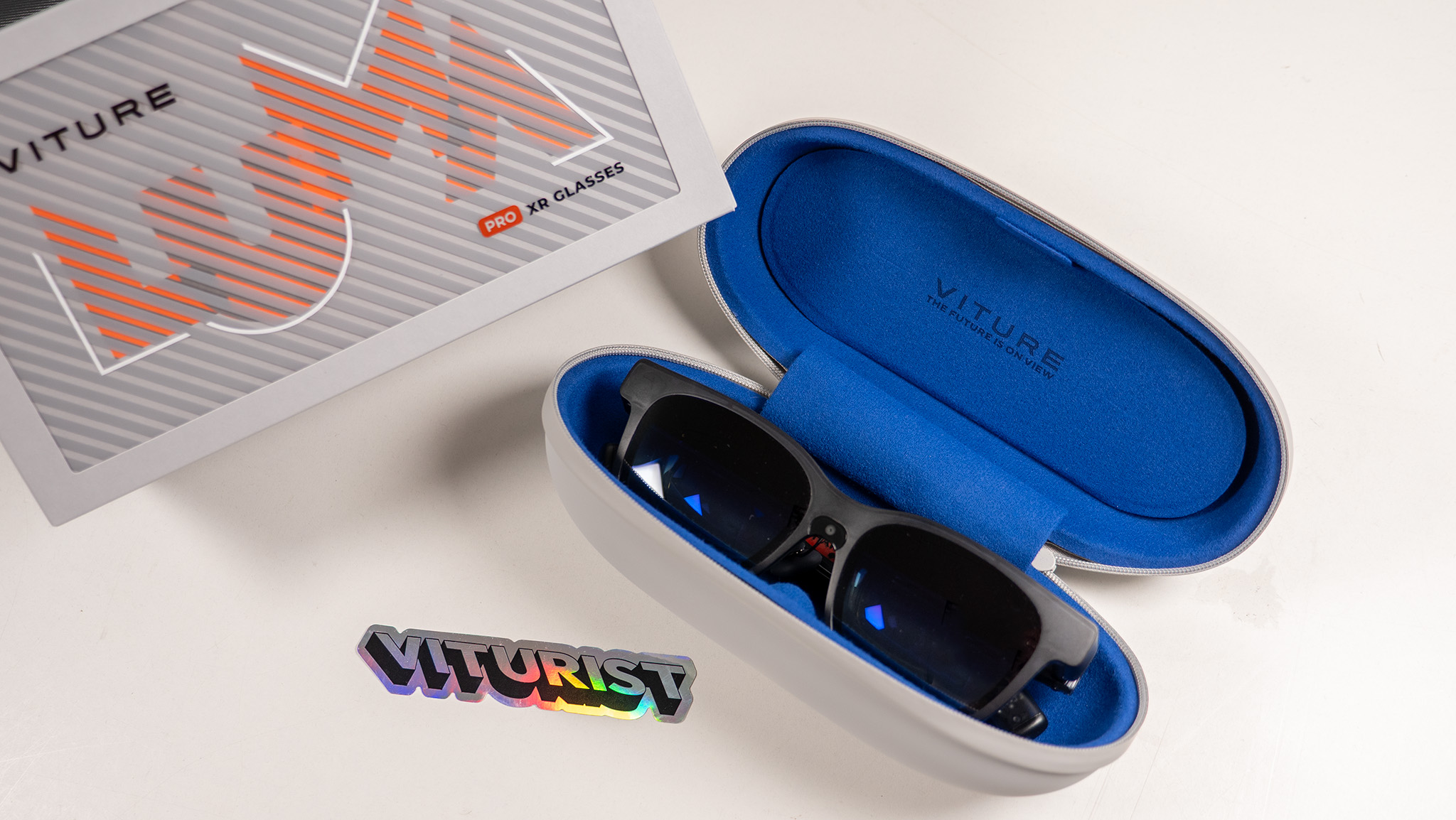 A pair of Viture Luma Pro smart glasses inside their blue felt-lined case, next to its box and a Viturist sticker