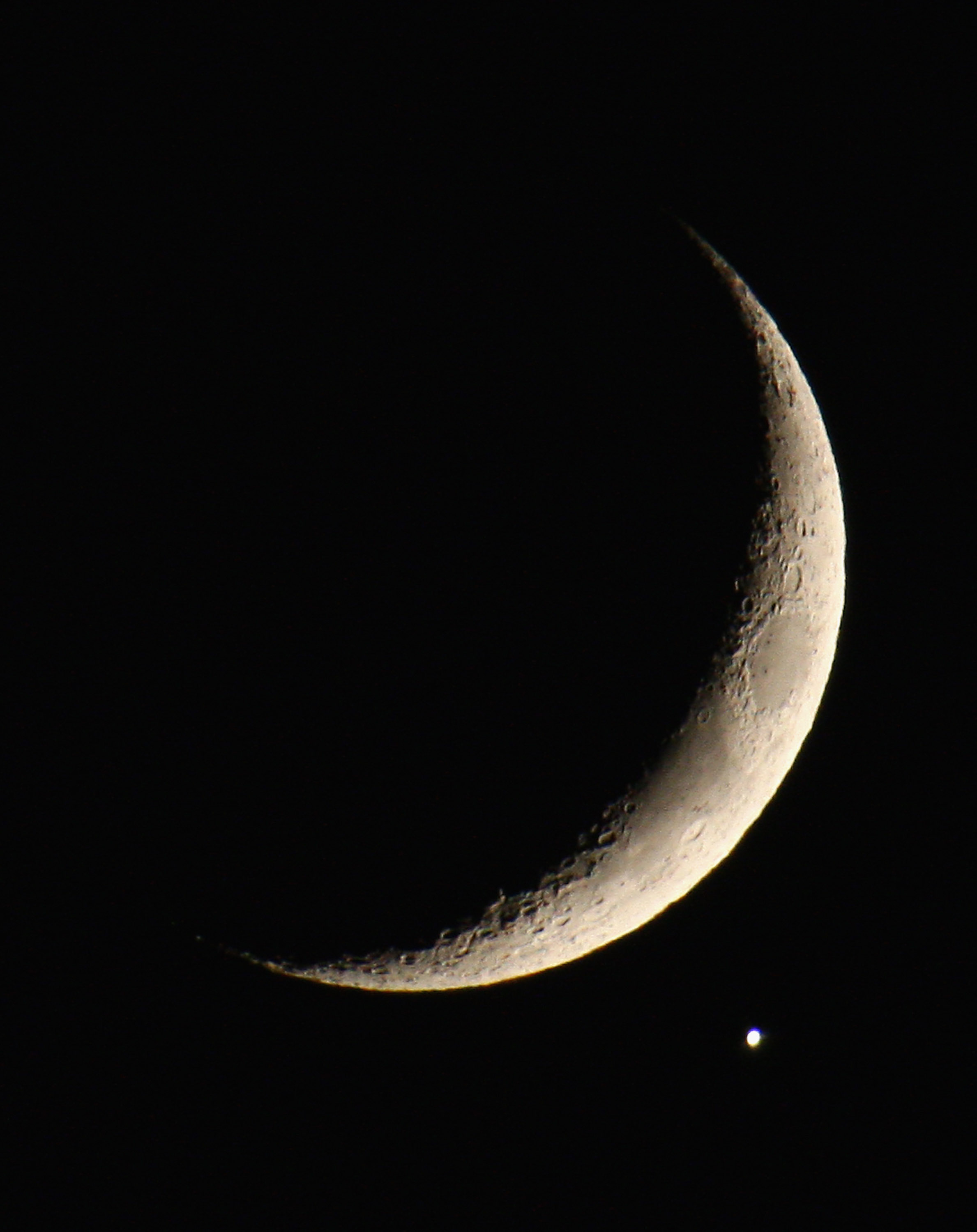 a thin crescent moon next to a bright pale yellow dot