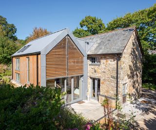 A double height pitched roof extension alongside a stone cottage clad in timber