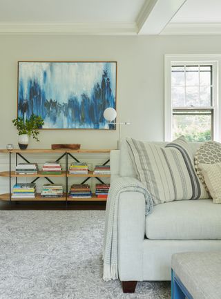 living room with white sofa and striped cushion and low display bookshelf with abstract blue painting above and grey rug