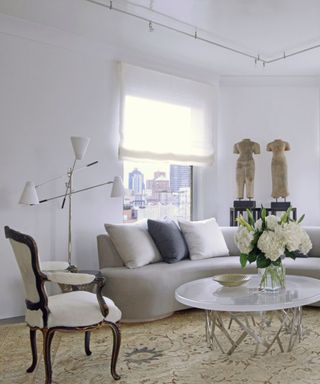 A white living room with a vintage armchair, sculpture, standing light fixture and curved gray sofa