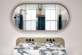 A white and black marble vanity with twin sinks and a large rounded mirror.