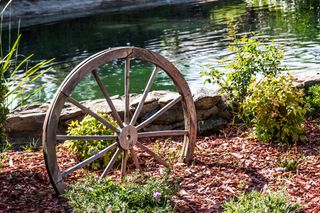 Old wooden wagon wheel In garden with rock wall and pond