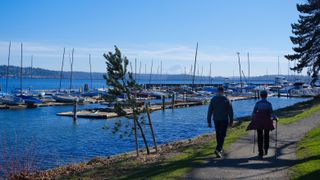 Scenic view of Lake Washington with two figures walking in the foreground in the shadows and boats, along with Mount Rainier visible in the background